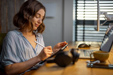 Young woman dressed casually having some creative work, drawing on a digital tablet, sitting at the...