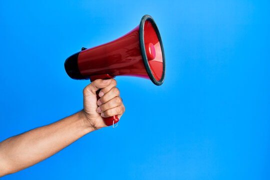 Hand of hispanic man holding megaphone over isolated blue background.