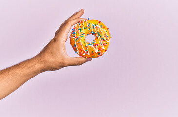 Fototapeta na wymiar Hand of hispanic man holding donut over isolated pink background.