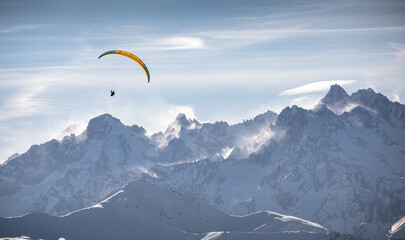 Parasailor glides over snowcapped mountains and lofty clouds