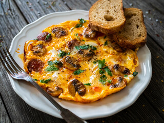 Delicious breakfast - scrambled eggs with fried champignon and chorizo on wooden table
