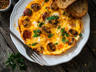 Delicious breakfast - scrambled eggs with fried champignon and chorizo on wooden table
