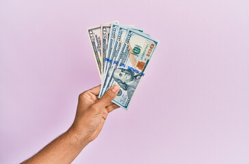 Hispanic hand holding usa dollars banknotes over isolated pink background.