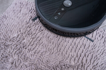 Robot vacuum cleaner on a gray carpet with a large pile close-up.