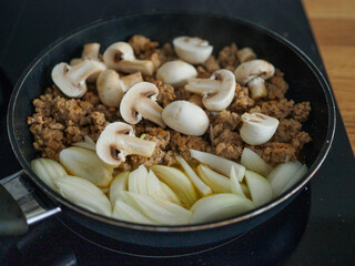 Pork minced meat in frying pan with onion, garlic and champignons
