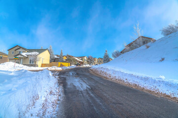Neighborhood road along snowy slope and houses against sunny blue sky skyscape