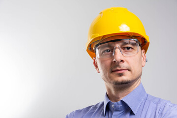Engineer with yellow helmet and jeans shirt near a industrial wall, inspiring confidence. 