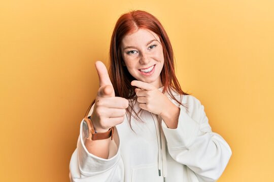 Young red head girl wearing casual sweatshirt pointing fingers to camera with happy and funny face. good energy and vibes.