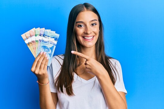 Young hispanic woman holding canadian dollars smiling happy pointing with hand and finger