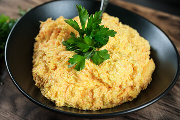 Tasty salad with carrots, grated cheese and mayonnaise for sandwich filling served on black plate on wooden table