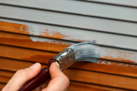 man's hand painting wooden panel door with a brush in lead grey colour
