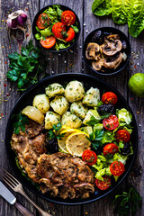 Fried pork steaks with lemon, boiled potatoes and vegetable salad served on wooden table

