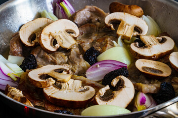 Pork steaks in frying pan with onion, garlic and champignons
