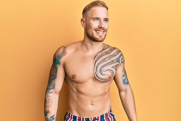 Fototapeta premium Young caucasian man wearing swimwear shirtless looking away to side with smile on face, natural expression. laughing confident.