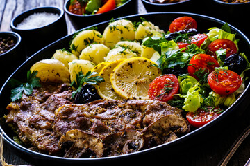 Fried pork steaks with lemon, boiled potatoes and vegetable salad served on wooden table
