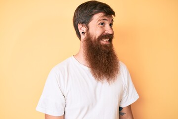 Obraz premium Handsome young red head man with long beard wearing casual white tshirt looking to side, relax profile pose with natural face and confident smile.
