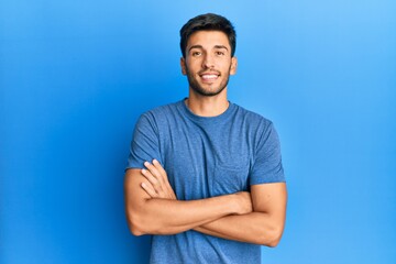 Fototapeta premium Young handsome man wearing casual tshirt over blue background happy face smiling with crossed arms looking at the camera. positive person.