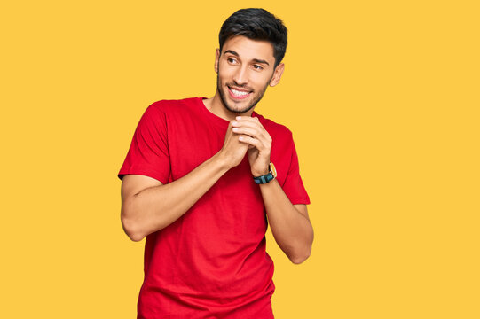 Young handsome man wearing casual red tshirt laughing nervous and excited with hands on chin looking to the side