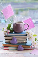 A cup of coffee, a stack of books, hearts and apple flowers on a wooden windowsill, the concept of romantic mood, reading, study, home comfort