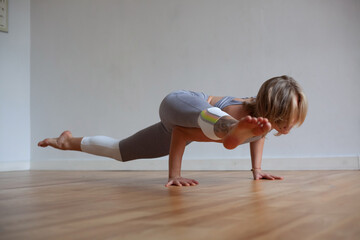 Sporty young woman practicing yoga, doing arm stand Astavakrasana, asymmetrical arm balance Pose on...