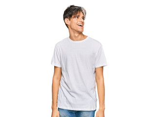 Young hispanic man wearing casual white tshirt looking away to side with smile on face, natural expression. laughing confident.