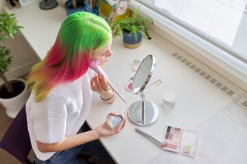 Teenager girl with dyed colored hair doing makeup looking in mirror