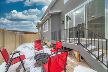 Snowy patio with fire pit and red chairs at the backyard of home on a cloudy day
