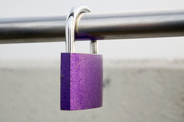A view of a purple padlock hanging on a metal pipe, close-up view