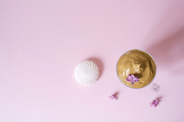 Beautiful dalgon coffee drink. Coffee mug with foam and lilac flower on a lilac pink background. Top view