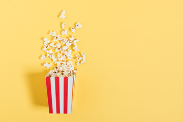 Red striped paper bucket with popcorn top view on yellow color background.