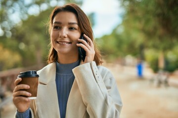 Young hispanic woman talking on the smartphone and drinking coffee at the park.