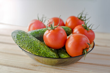 a plate with fresh vegetables from the vegetable garden such as tomatoes and cucumbers on a wooden table.
