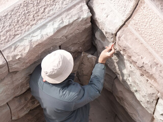 Audgrabungsst&auml;tte und Bauarbeiten mit M&ouml;rtel und Spachtelmasse an einem sandig beigen Steinfundament. Arch&auml;ologe mit Schlapphut arbeitet in der Sonne mit Pinsel und Spachtel.