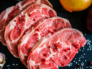 Raw pork chops with onion garlic and seasonings on plate on wooden table
