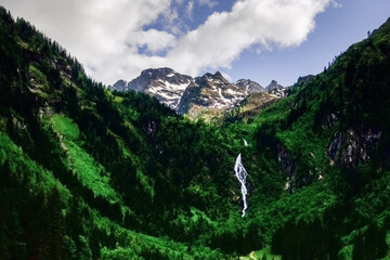 beautiful high waterfall in green mountains while hiking