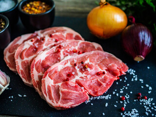 Raw pork chops with onion garlic and seasonings on plate on wooden table
