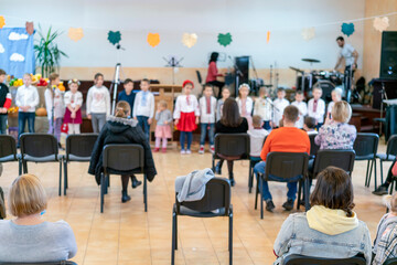 Parents at the performance of children in kindergarten or school. Children on stage. Many parents are watching the kids performance in the hall during Chistmas holiday, blur