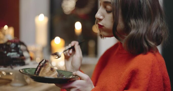Woman savoring festive chocolate cake sitting by the table during a celebration at home. Eating sweets on a holidays concept