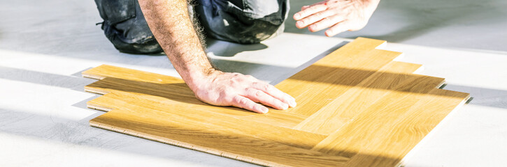 worker installing oak herringbone parquet floor during home improvement