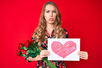 Young caucasian woman with blond hair holding heart draw depressed and worry for distress, crying...