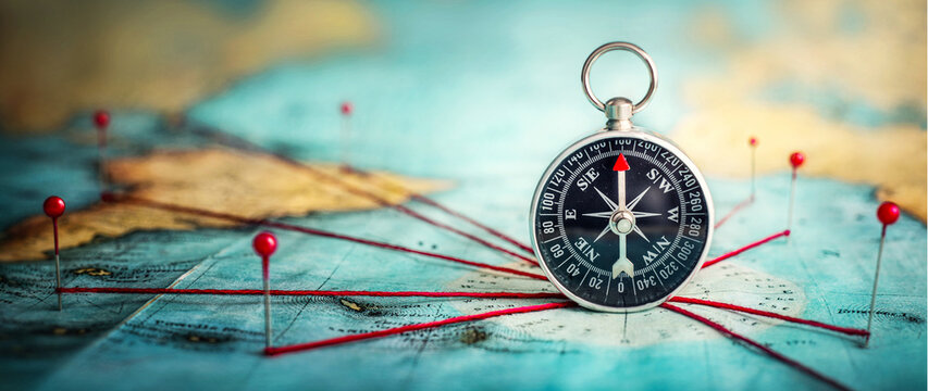 Magnetic compass  and location marking with a pin on routes on world map. Adventure, discovery, navigation, communication, logistics, geography and travel theme concept background.. Macro photo. 