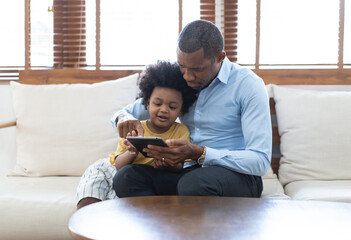 Portrait of happy African American father and son using a tablet while sofa sitting on sofa at...