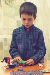 The boy playing an electric constructor. The child is played by intellectual toys. A boy in a blue shirt masters electronics. The concept of early development of children. vertical photo. toned
