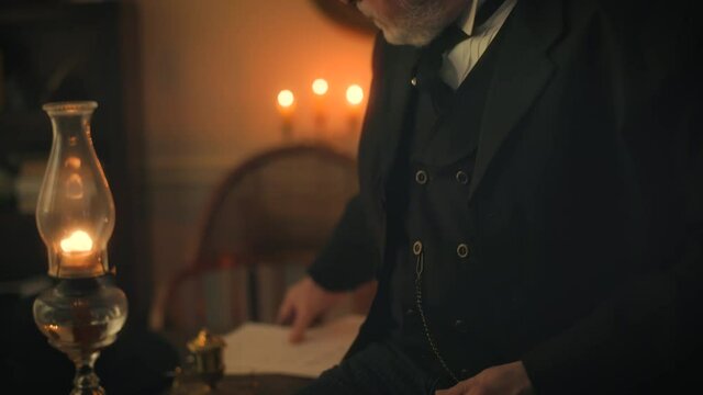 A mature pensive businessman from the Victorian era sitting on the edge of his desk who checks his pocket watch as the scene pans up to reveal him picking up a document and reading it.