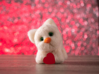Fototapeta premium white toy cat stands on the table with a red heart on a pink background