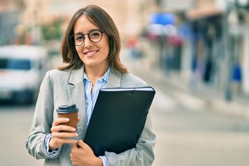 Young hispanic businesswoman drinking coffee holding binder at the city.
