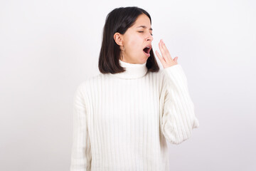 Young brunette woman wearing white knitted sweater against white background being tired and yawning after spending all day at work.