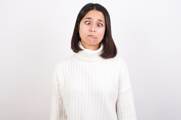 Young brunette woman wearing white knitted sweater against white background making grimace and crazy face, screaming out of control, funny lunatic expressing freedom and wild.