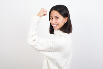 Portrait of powerful cheerful Young brunette woman wearing white knitted sweater against white...