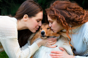 Two redhead, ginger women, sisters kissing their collie dog. Lesbian couple of girls